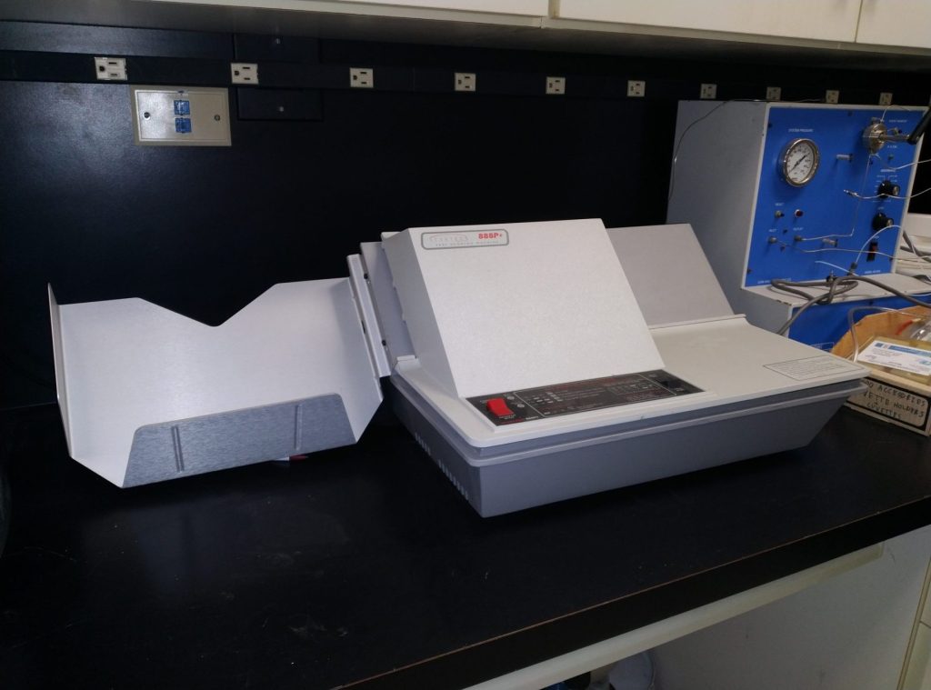A photograph of the Scantron machine at La Sierra University's chemistry lab. The machine is large and bulky, made of white plastic. 