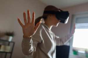Selective focus shot of teenage girl standing in her room, with outstretched arms, gesturing as if she is touching something in a game she is playing with a virtual reality stimulator.