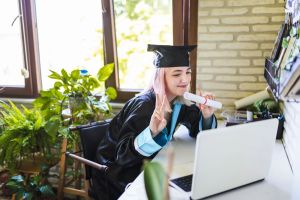 Teenage girl wearing graduation gown and cap greeting her family on video call