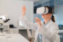 A photograph of a female student in a lab coat wearing a VR headset and holding up her hands.