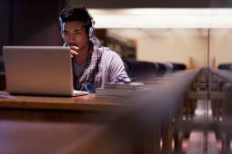 A student in a library looks at his laptop with headphones on at night.